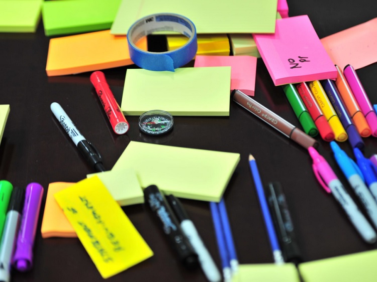 Sticky notes, colorful pens, a plastic compass and painters tape on a table.